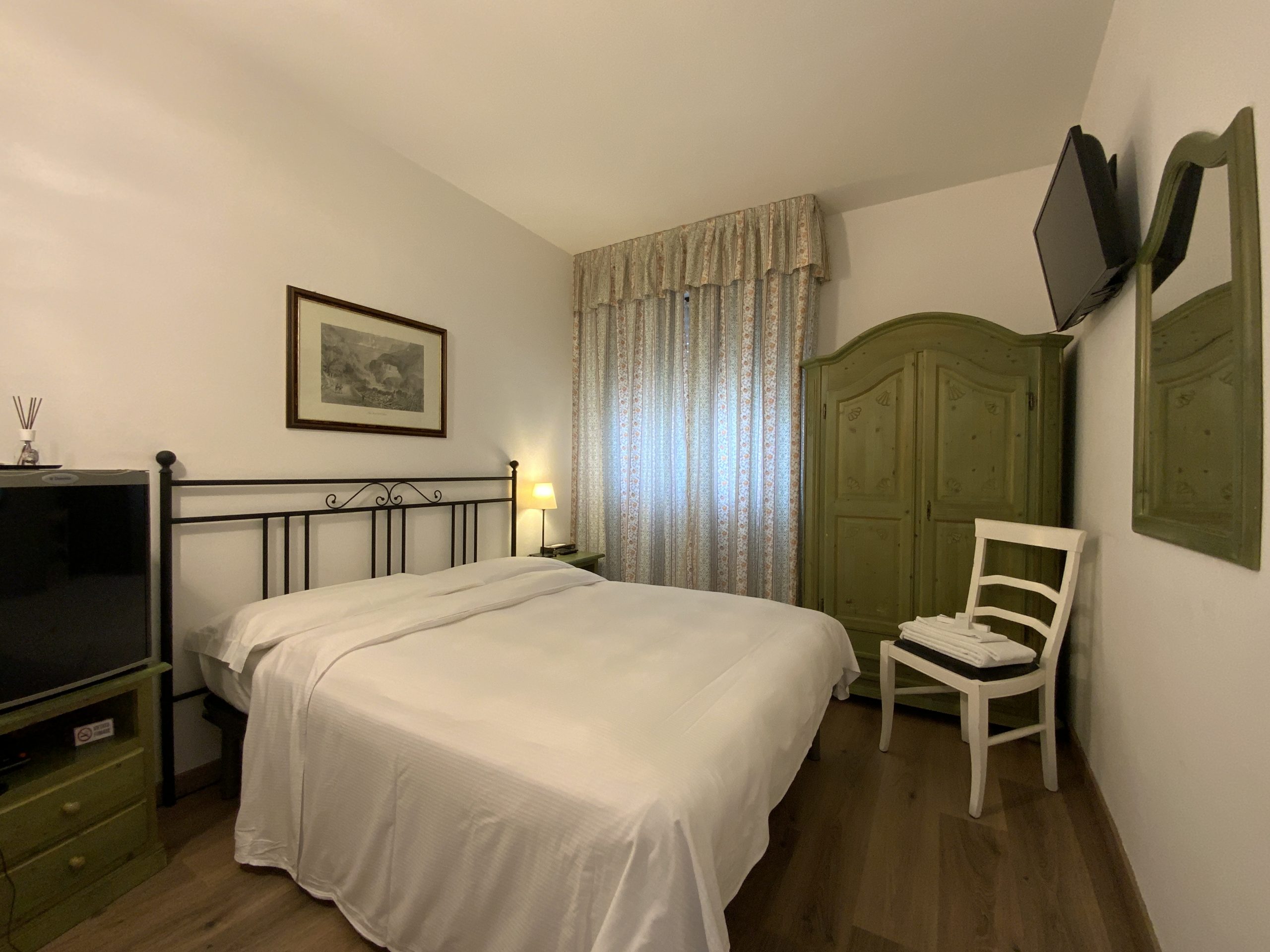 vista dell'intera classic room. il letto matrimoniale ha la testata in ferro battuto nero e si può vedere il frigo bar a fianco. si vede la tv e l'armadio